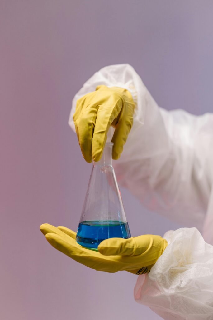 Close-up of gloved hands holding a flask with blue liquid in a laboratory setting.